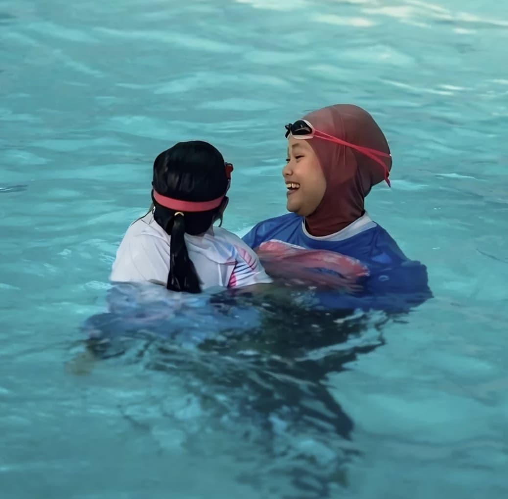 Pelatih Tumbuh Kembang Aquatic tertawa bersama anak di kolam